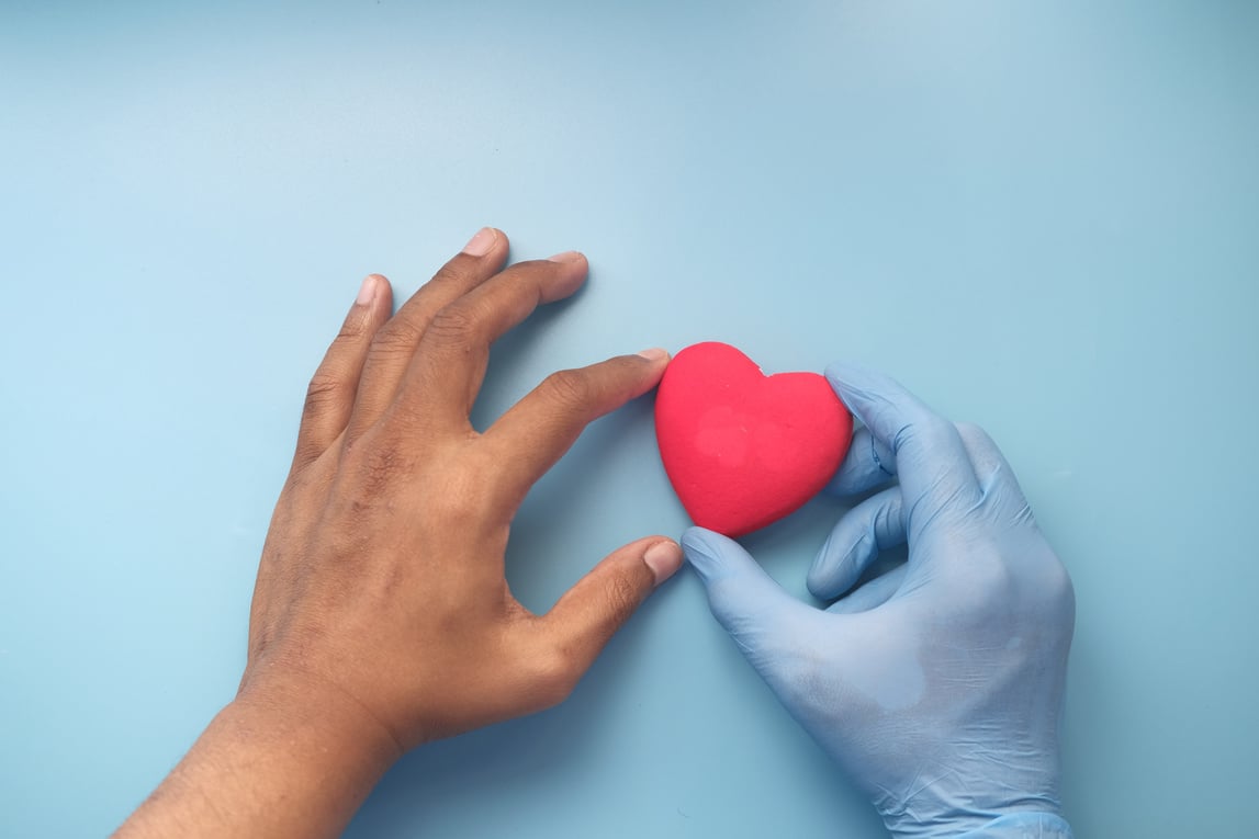 Man Hand in Protective Gloves Holding Red Heart on Blue